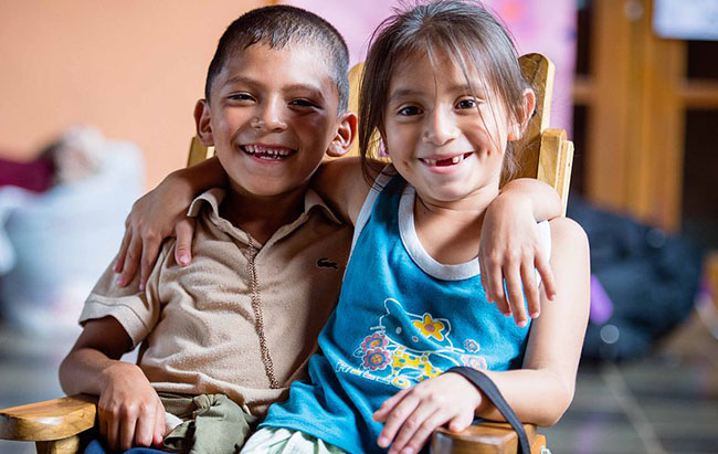 Two children smile for the camera, arms over each other's shoulders