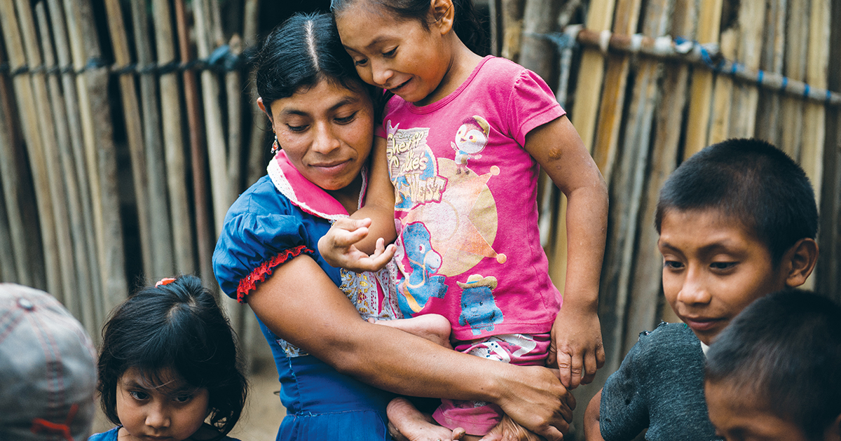 Mother holds her daughter outside of their dilapidated home.