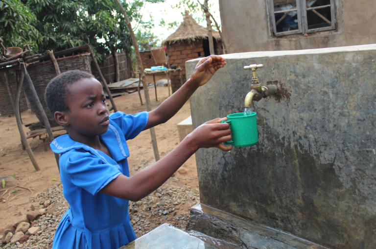 A girl fills her cup with water from a spigot