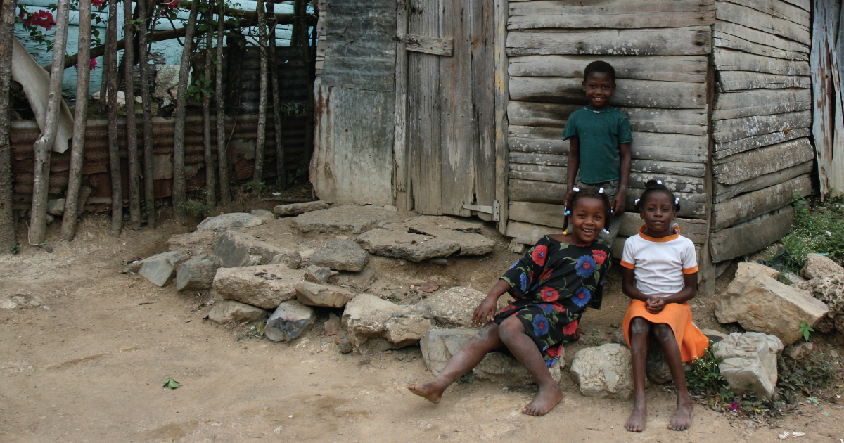 Vulnerable children sit outside a rundown house