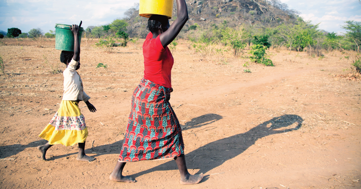 A woman and girl carry safe water in buckets on their heads in Zambia
