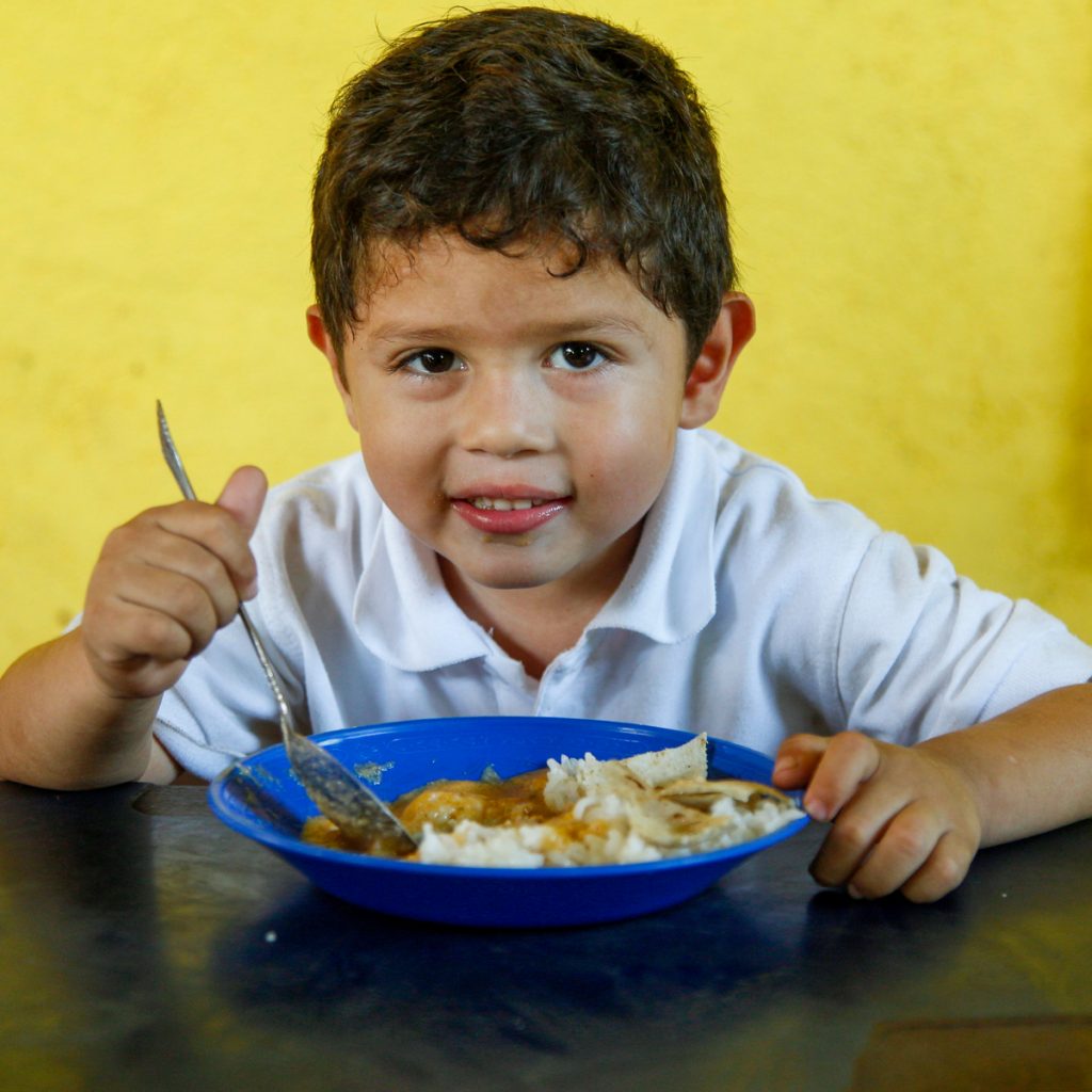 A child smiles while eating out of a blue bowl