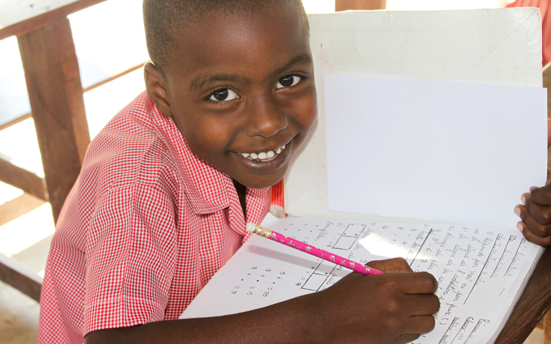 Boy writing in notebook and smiling to the camera