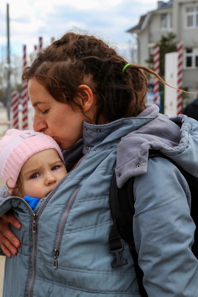 Ukrainian woman fleeing with her child. The baby girl looks at the camera while her mom kisses her head