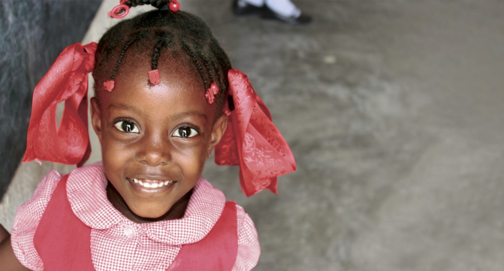 A school girl dressed in pink smiles for the camera, grateful for those who give to help