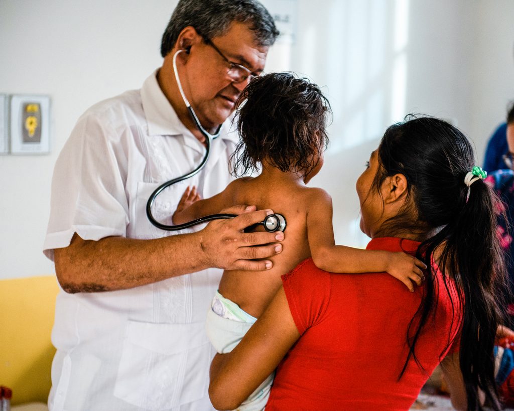 A doctor tends to a child while a woman holds the little one
