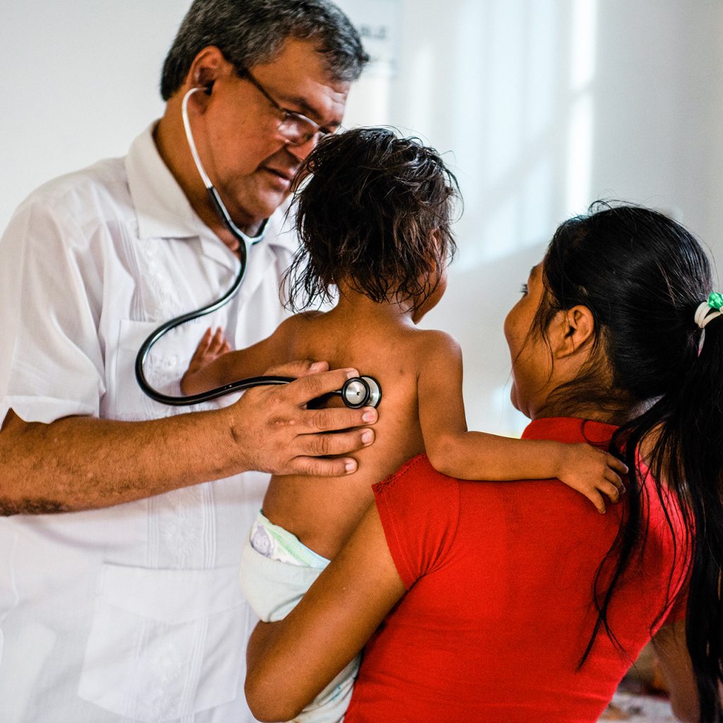 A doctor tends to a child while a woman holds the little one