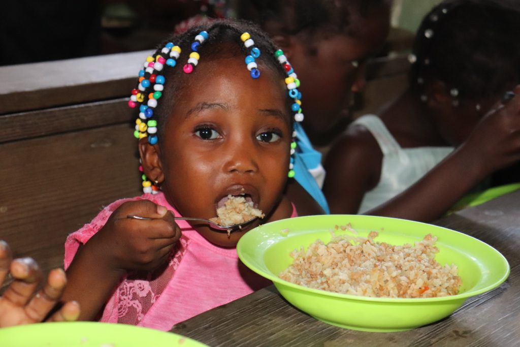 Haitian girl looking at the camera while eating her lunch