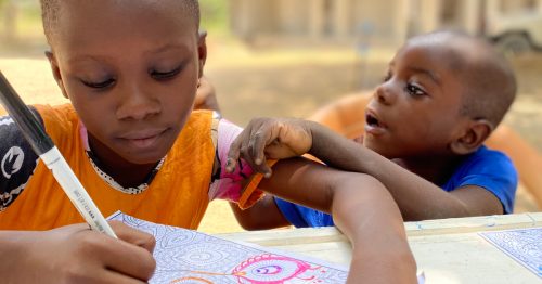 Kenyan girl coloring a book while boy looks at her