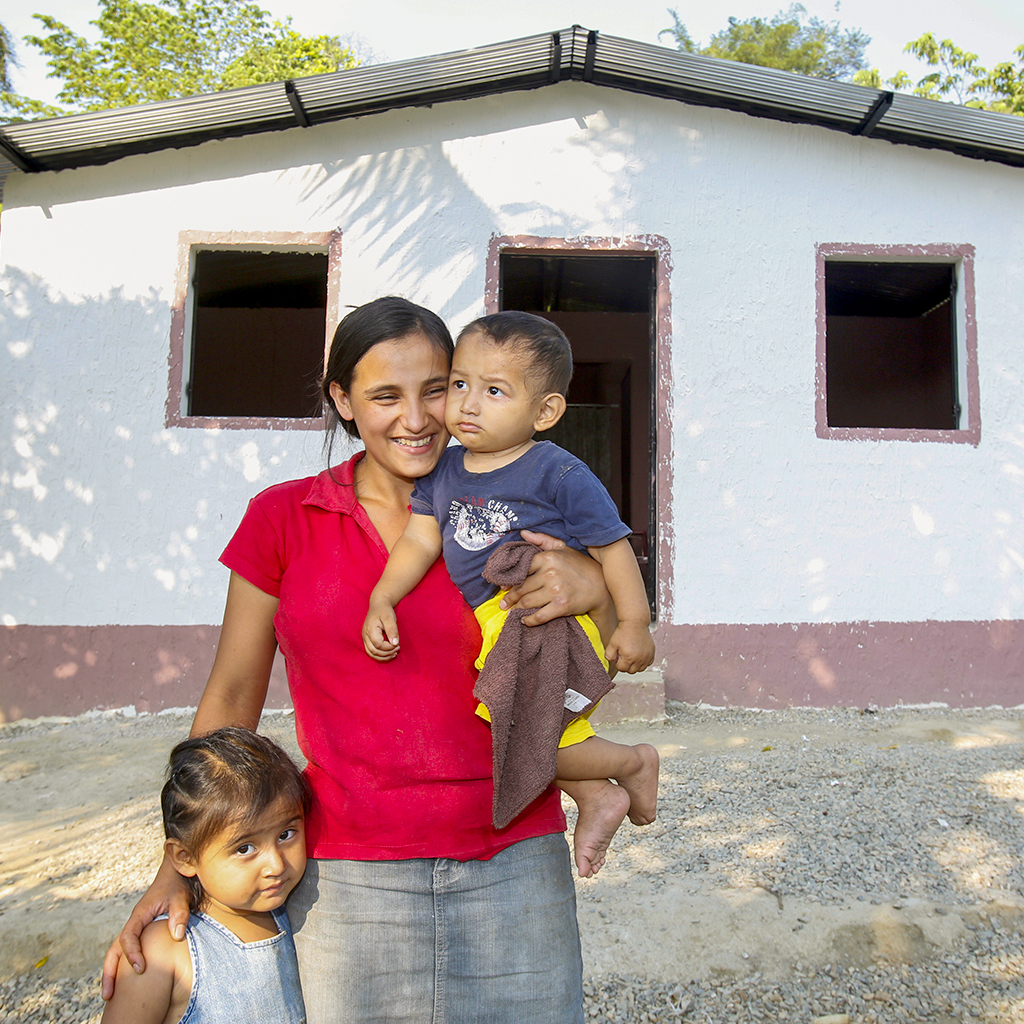 Mother with her 2 children, smiling in front of her new house