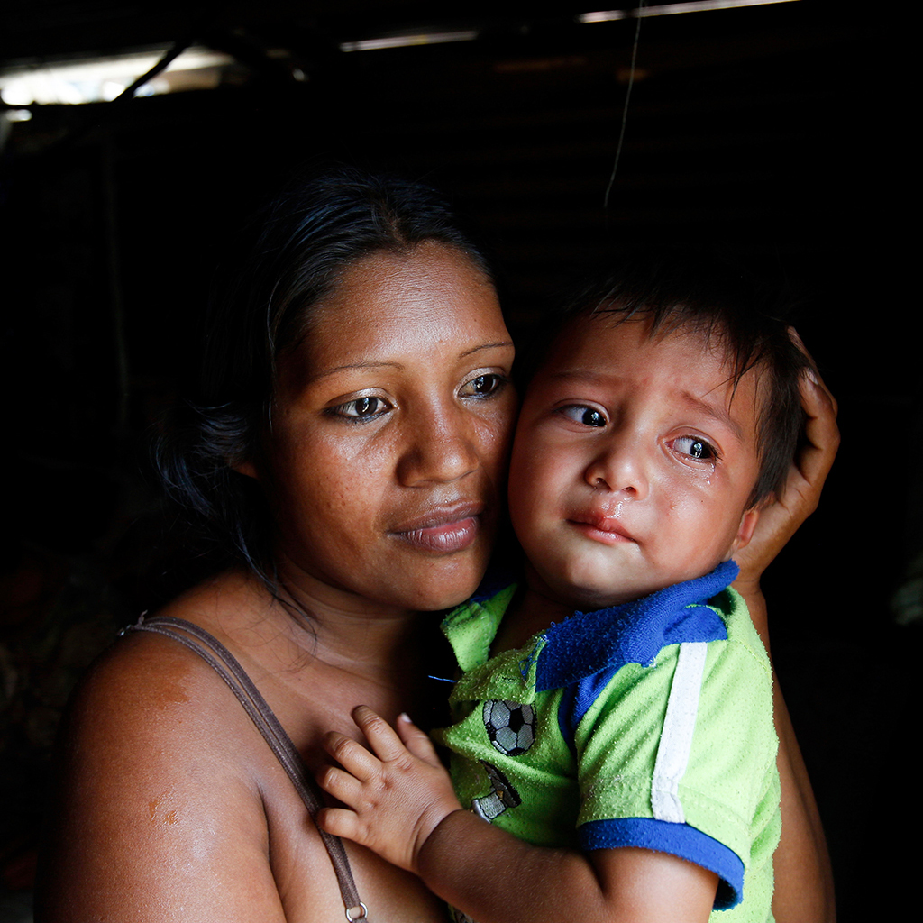 A mother holds her child in a darkened room