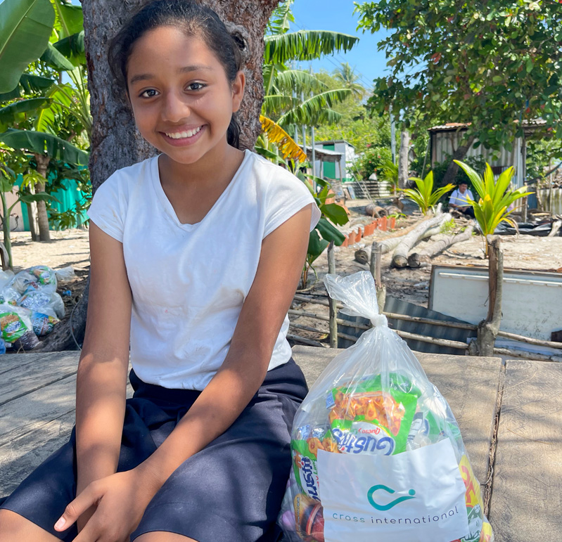 Maria Fernanda, a 13-year-old girl wearing her school uniform, smiling to the camera after receiving a bag of food for her home.