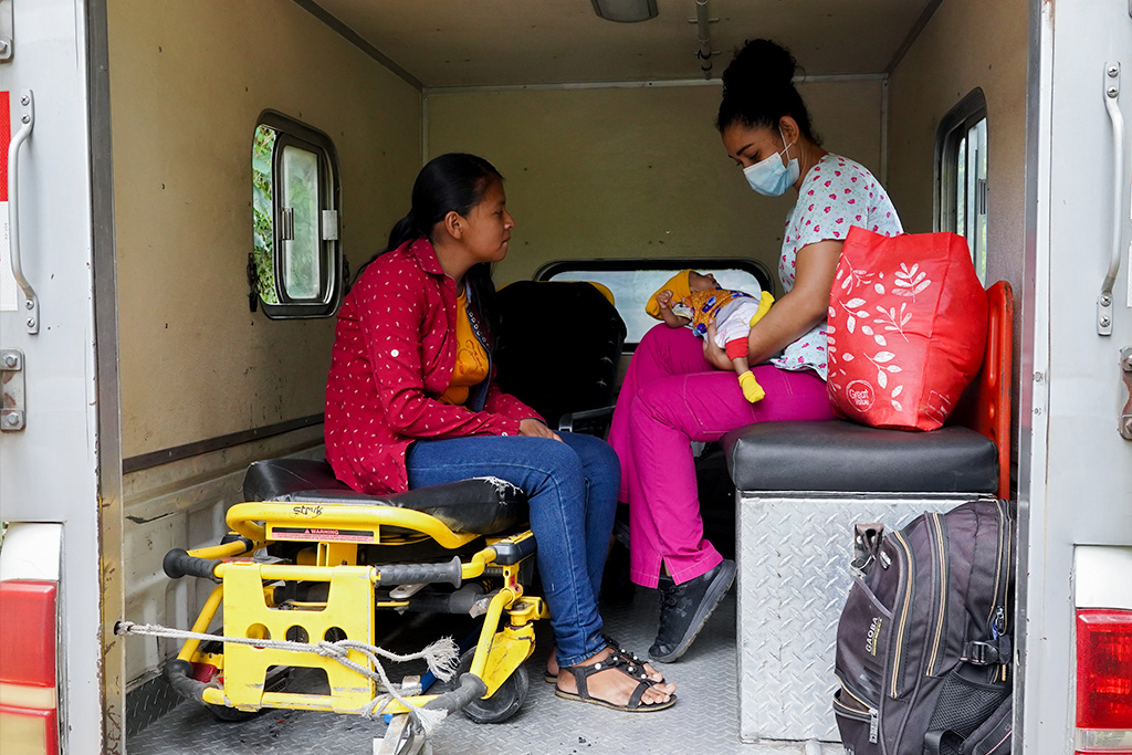 Nurse Hosmary in the ambulance, carrying baby Yeimi while her young mother sits in front of them