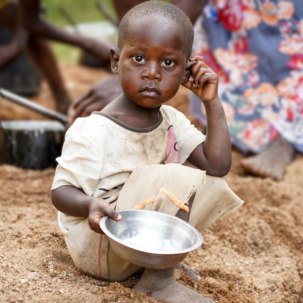 A young Zambian boy holds an empty bowl hoping for food