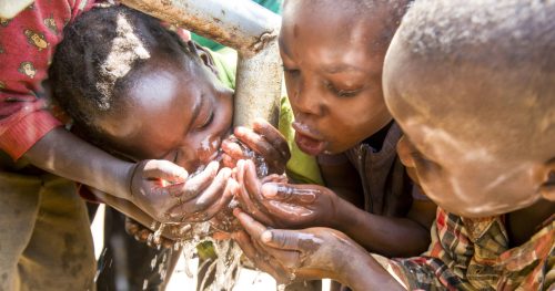 Zambian children gleefully crowd around a newly constructed borehole and water pump, their faces alive with joy as they touch, drink, and revel in safe water for the first time in their village.