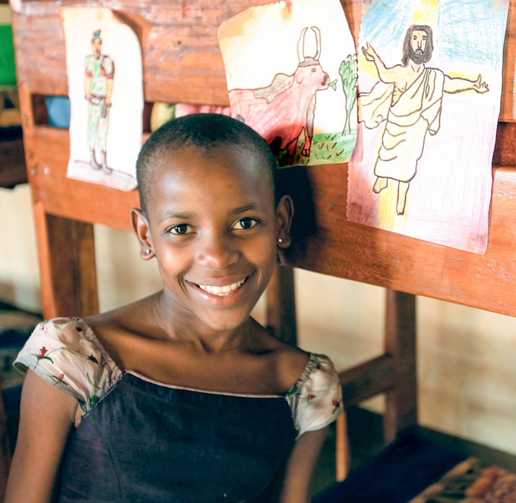 Ugandan girl smiling in front of her drawings