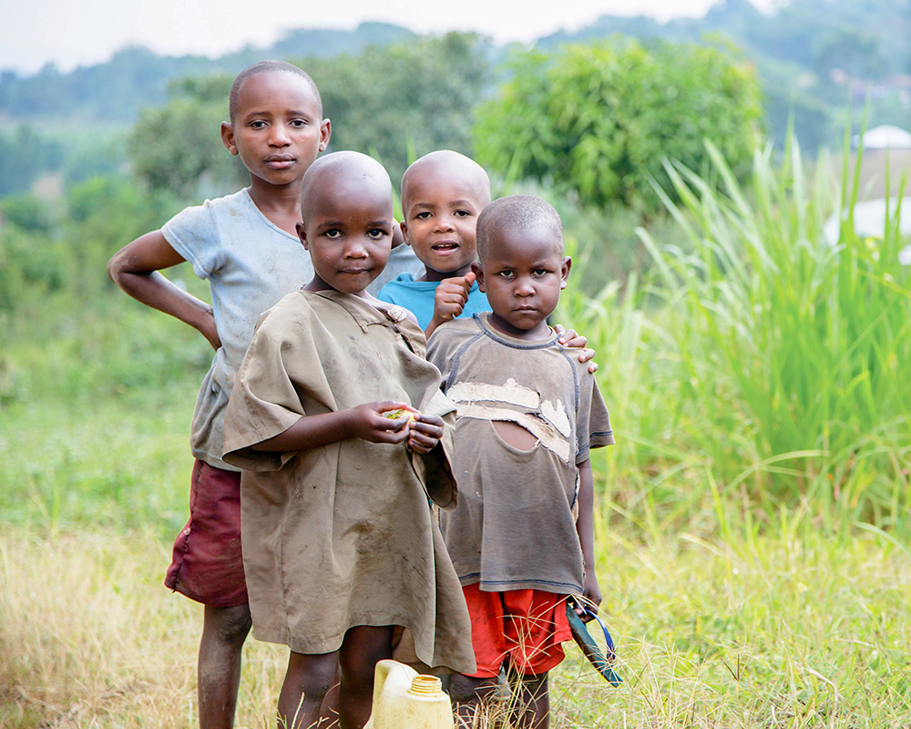 Four Ugandan children in the fields standing together and looking at the camera