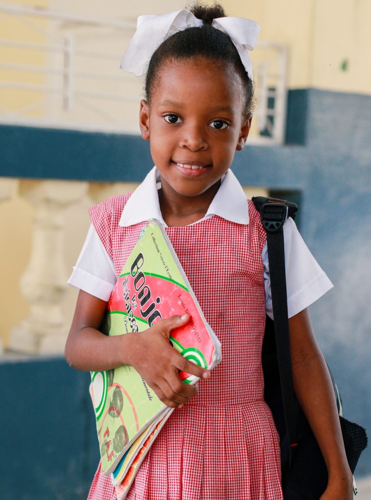 Happy 7-year-old girl in uniform with backpack and school book, excited and ready for a day of learning.