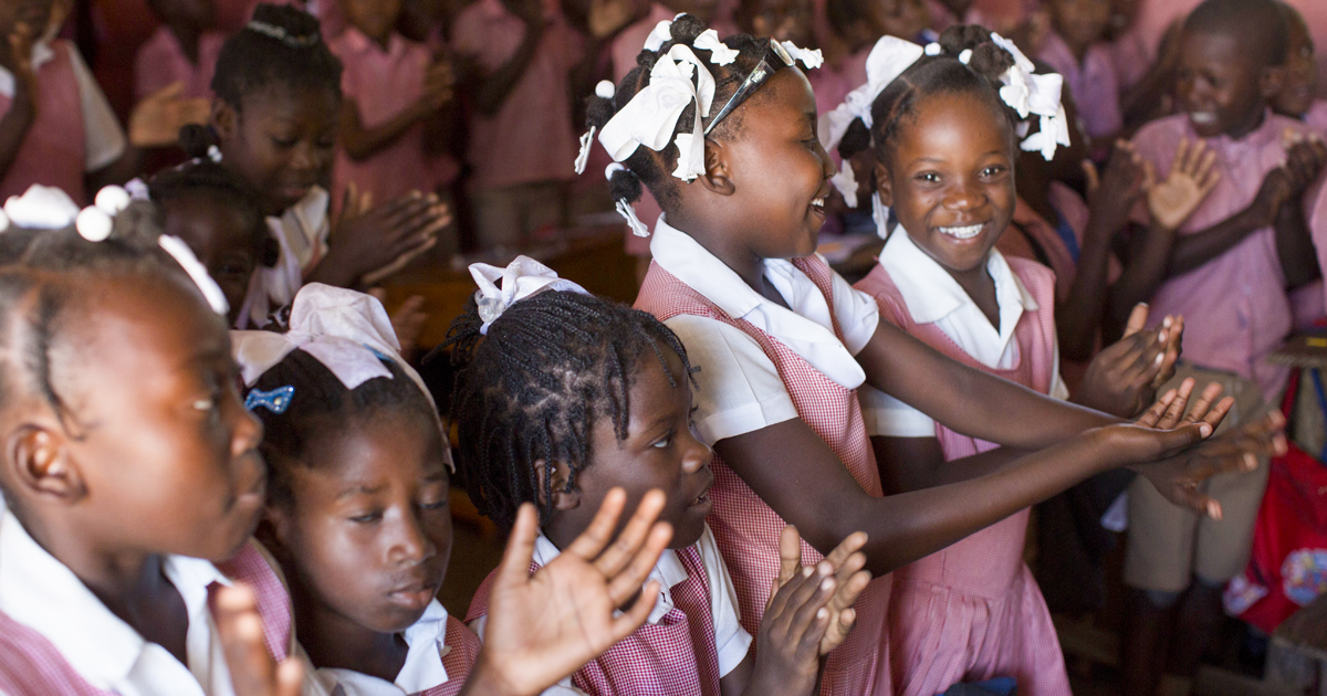 Group of Haitian children in a classroom smiling and clapping during a fun, interactive lesson.