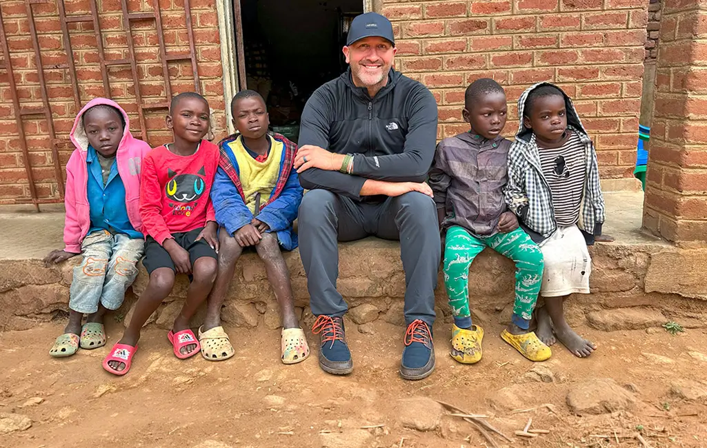A Cross International leader sits alongside children in a community served through long-term partnership.