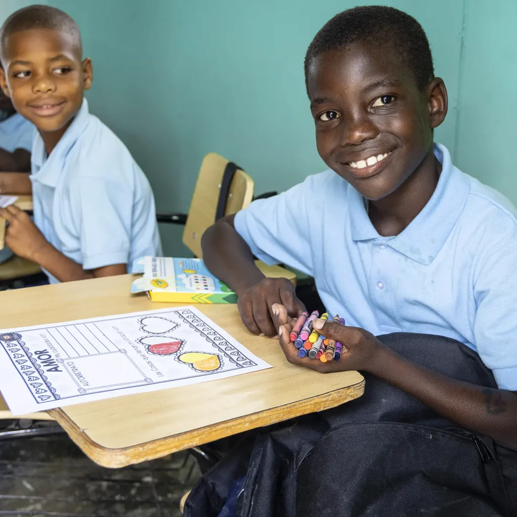 School-aged child smiles while working with crayons in a classroom.
