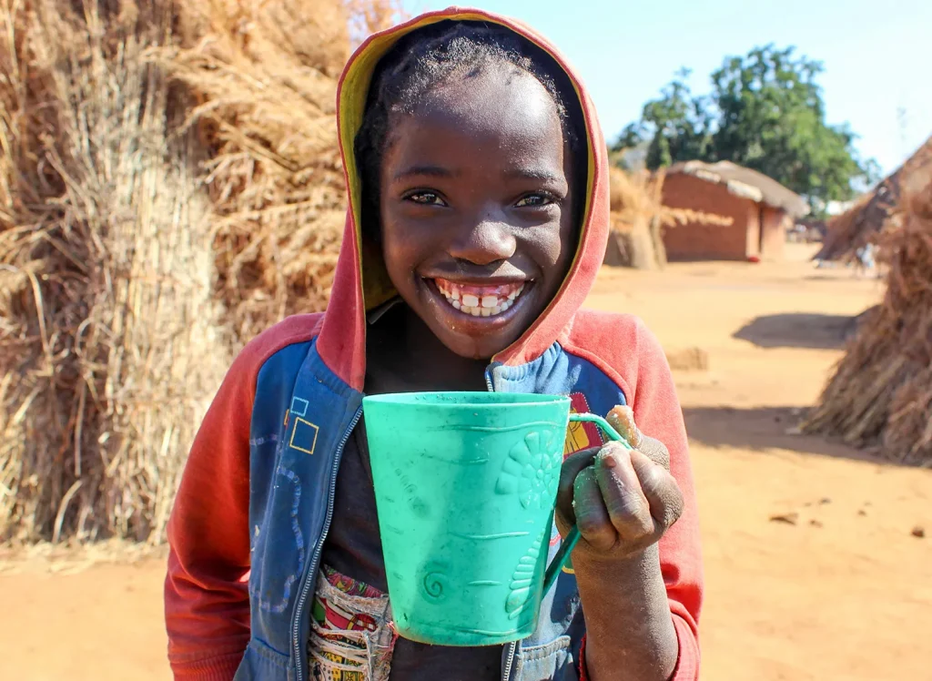 Zambian girl smiling to the camera while drinking a cup of water