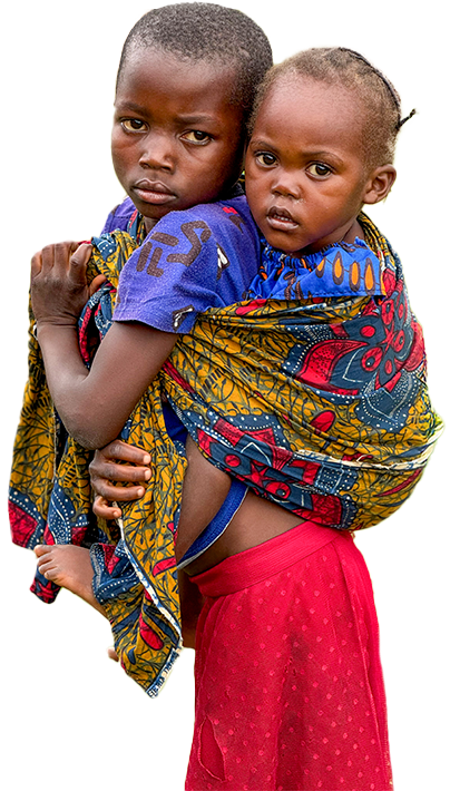 Young child stands on grass carrying a baby on their back secured with a colorful patterned cloth.
