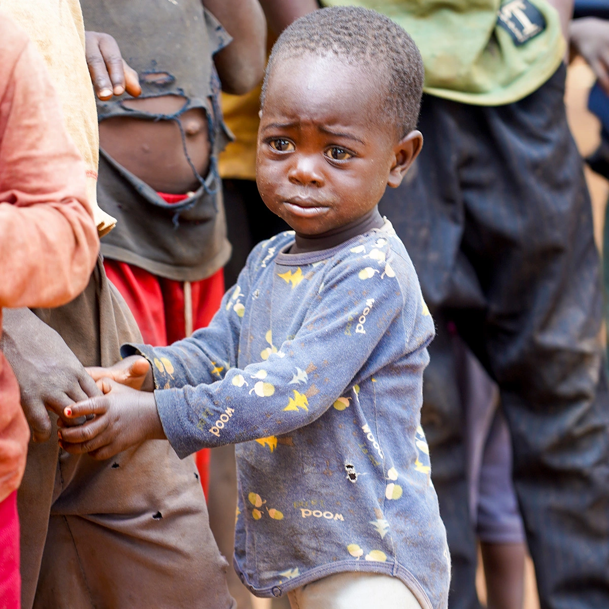 Young child stands beside an adult, looking concerned while holding the adult’s hand.