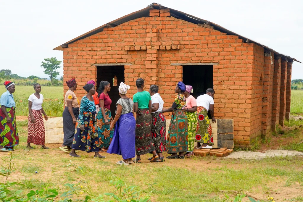 Group of women gathered outside a small brick church in a rural community near the entrance.
