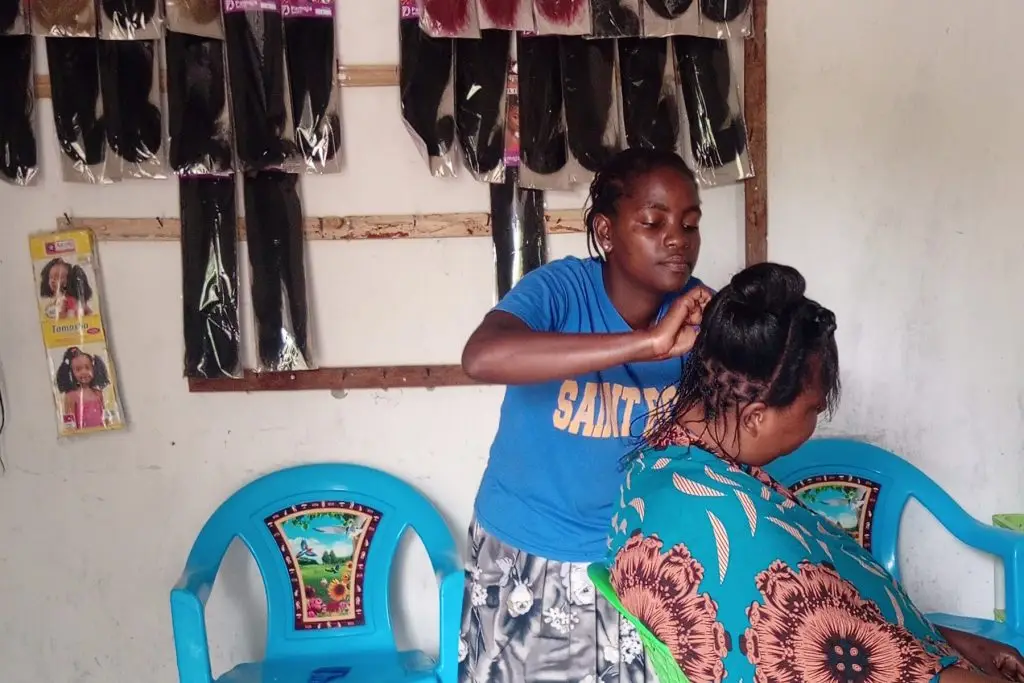 A stylist styles hair for a client sitting in a chair.