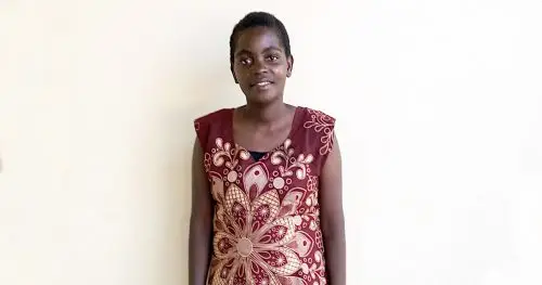 A young woman stands against a white background wearing a beautiful dress.