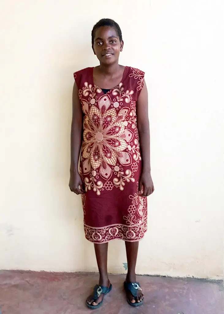A young woman stands on a white background wearing a beautiful dress.