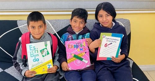 Three children sitting on a couch holding school notebooks, smiling in a learning environment.