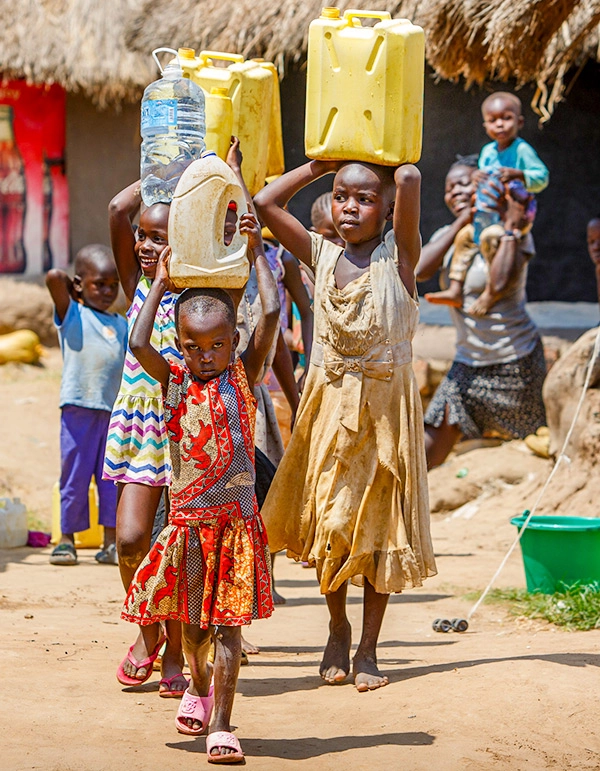 Children carrying water jugs on their heads through village