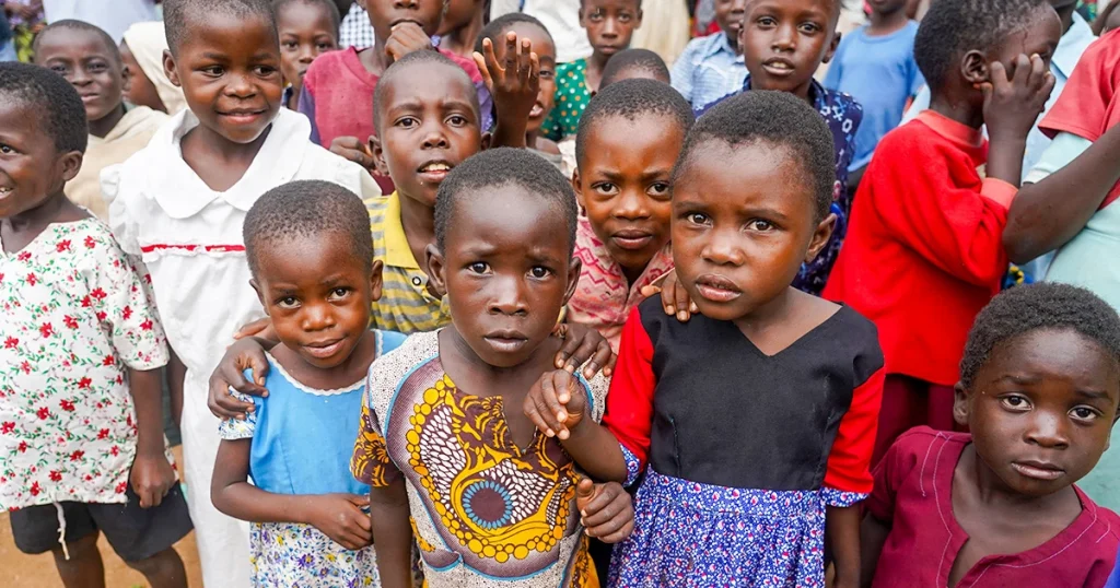 Group of young children standing closely together outdoors, many looking at the camera.